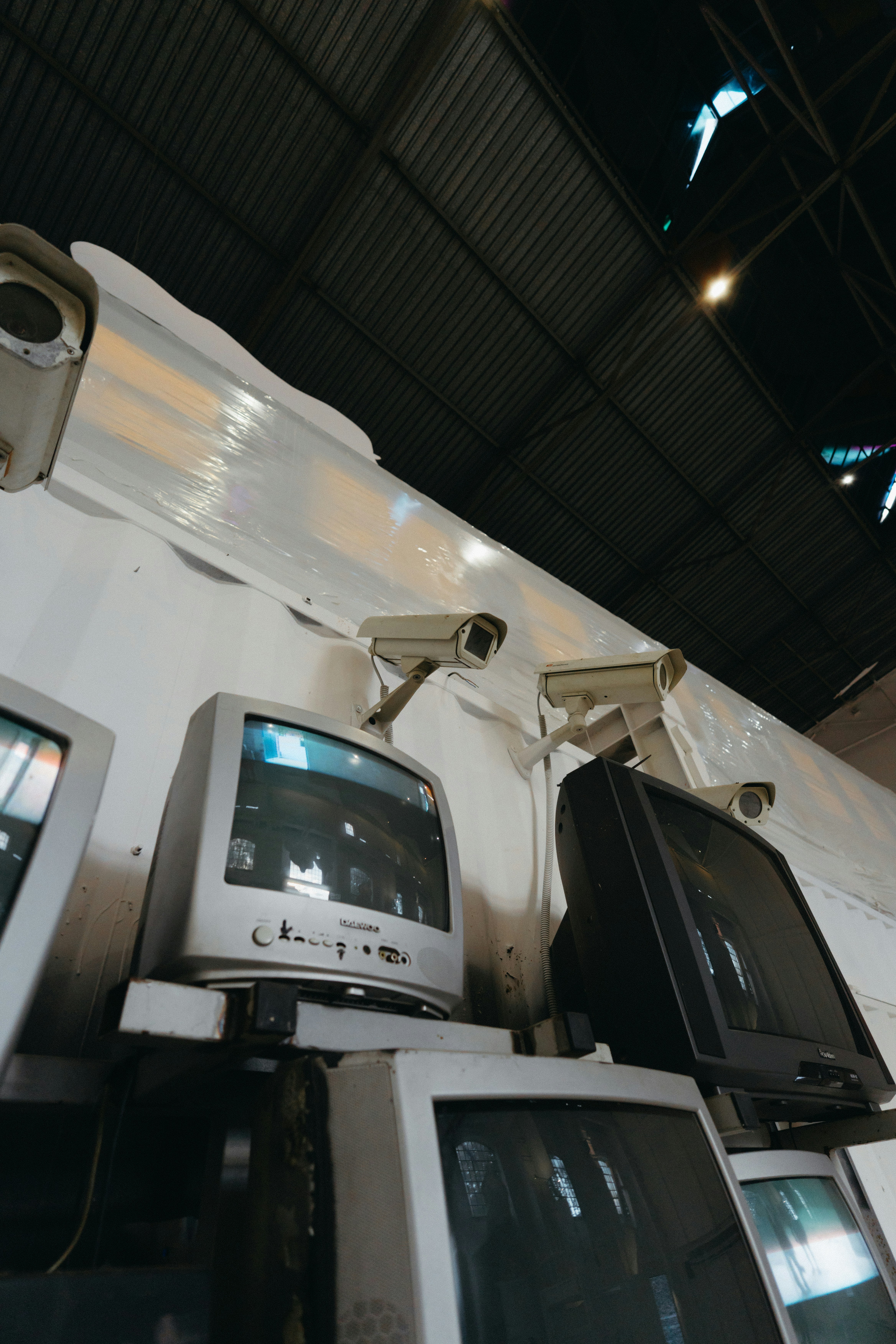 📜 The Evolution of Affordable Flat Screens: A Brief History by TV Brands Old crt monitors and security cameras under a dark ceiling.